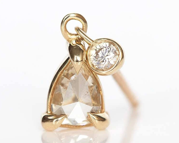 Pear shaped diamond hanging from a single stud earring set in yellow gold