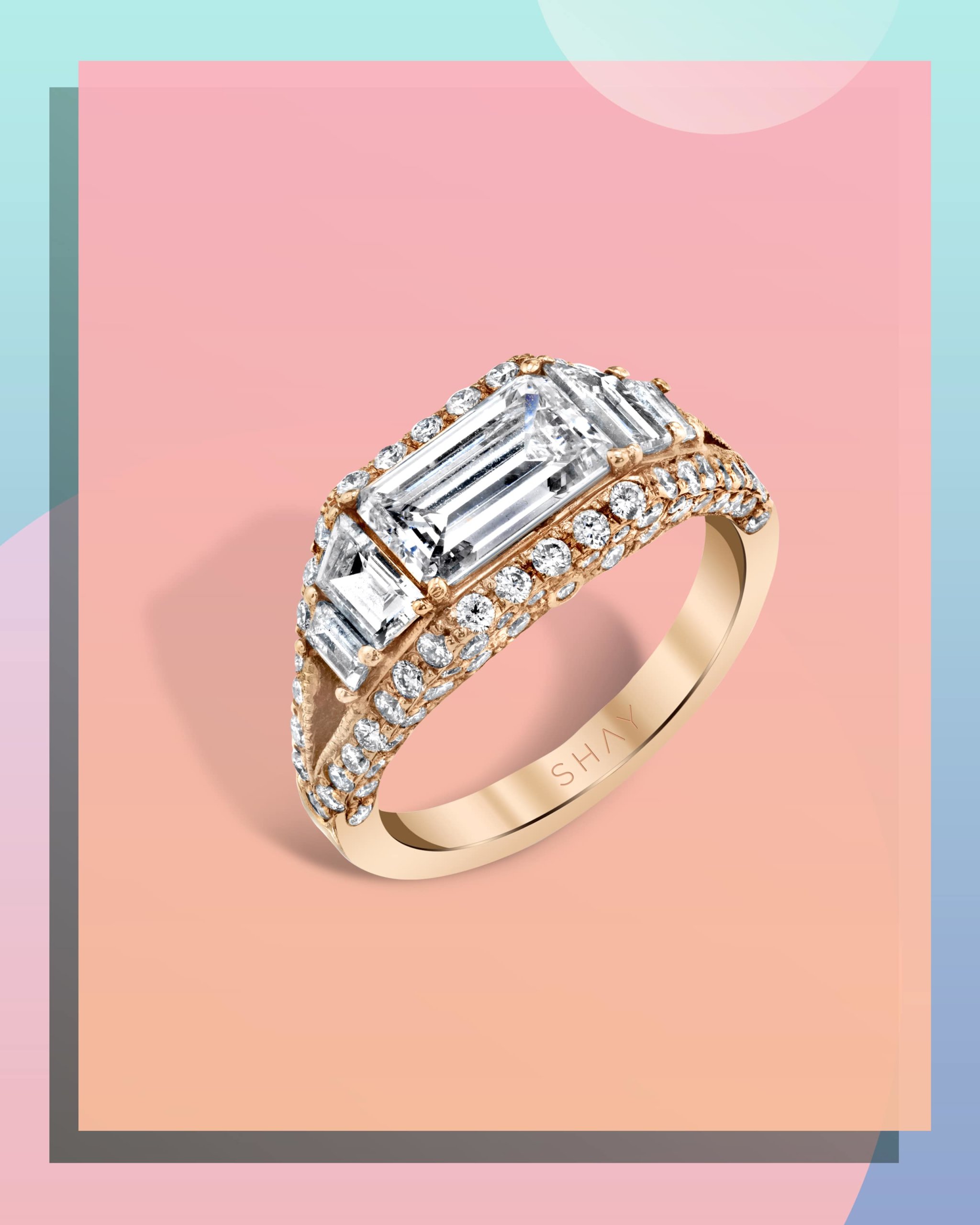 Emerald cut diamond hugged by white diamonds set within an east west engagement ring on a yellow gold band from Shay Jewelry
