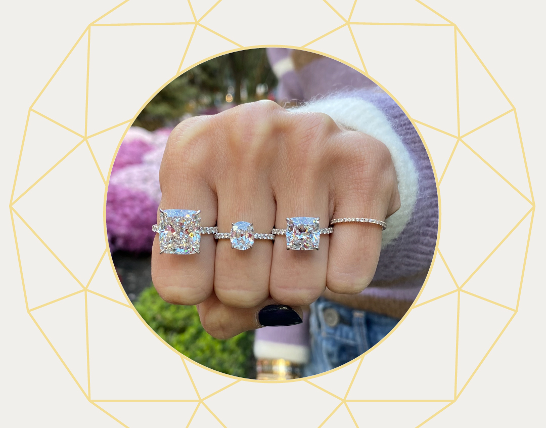 Hand featuring two custom cushion cut diamond rings with pave bands, oval cut diamond custom engagement ring, pave diamond ring by Stephanie Gottlieb