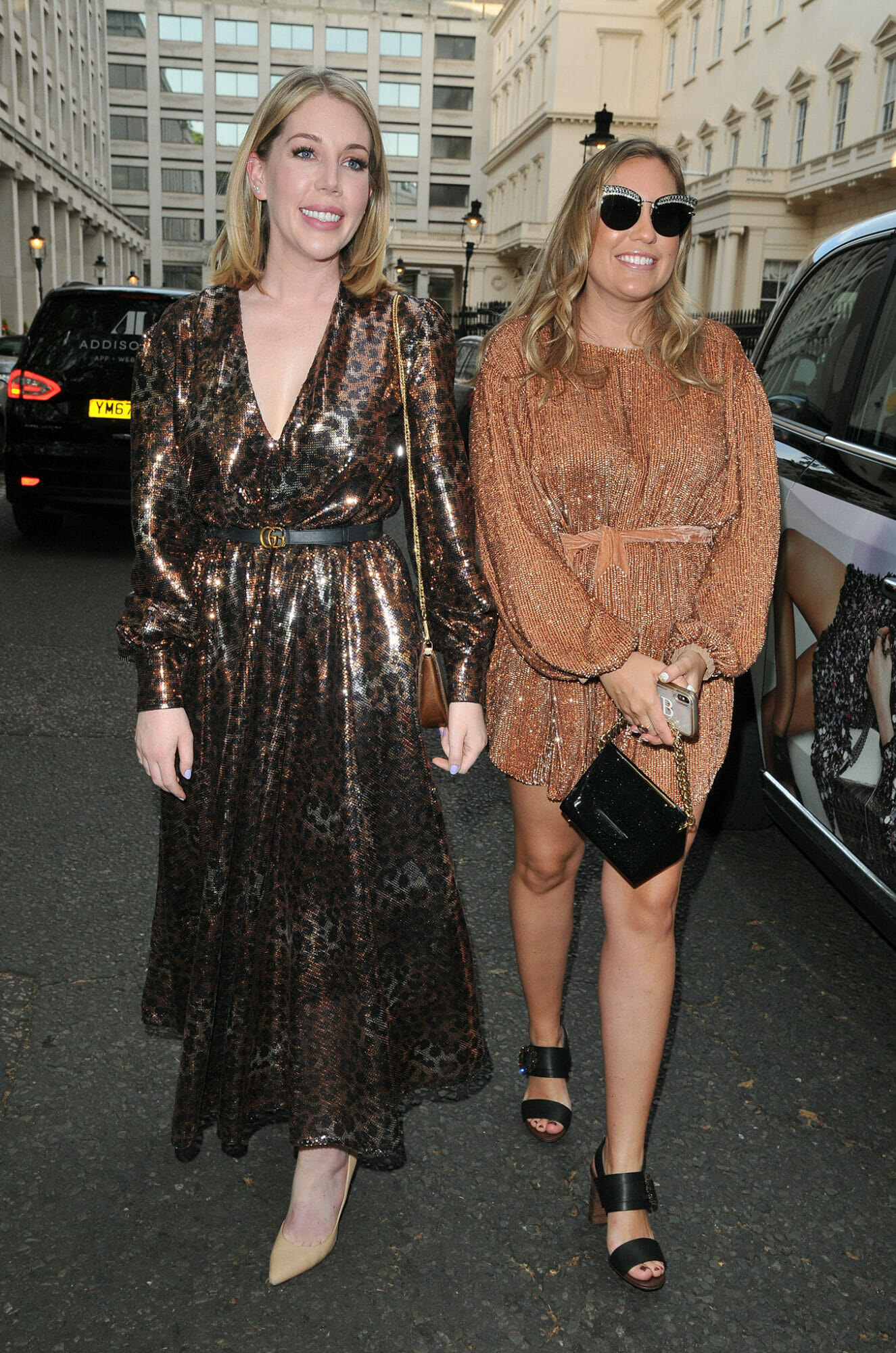 Katherine Ryan on the left smiling and Jennifer Machalski-Bray on the right wearing sunglasses both waling on the street wearing heels