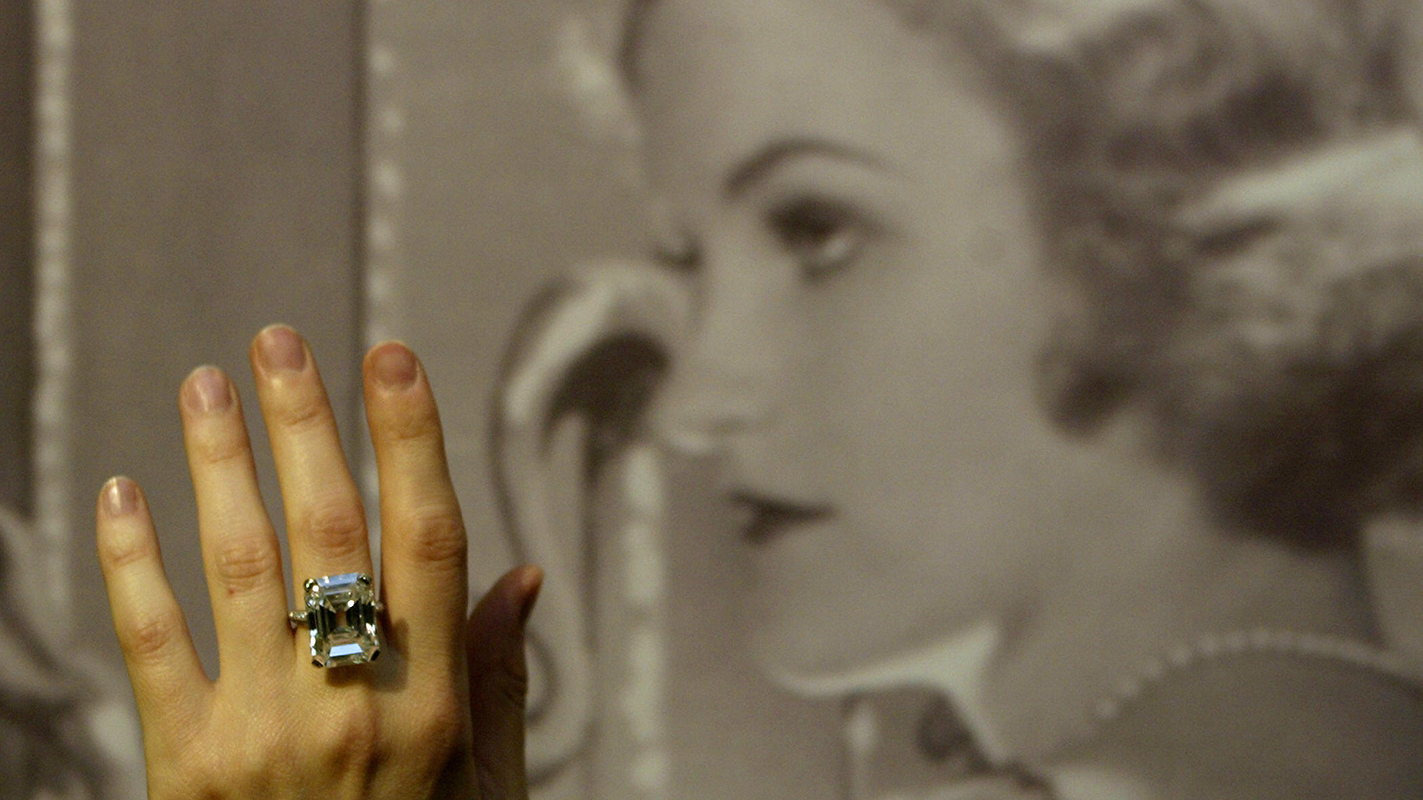 An assistant at Christie's auction house displays a 19.72 carat diamond ring made by Tiffany & Co. owned by heiress Doris Duke, pictured in background, 04 May, 2004. (Getty Images)