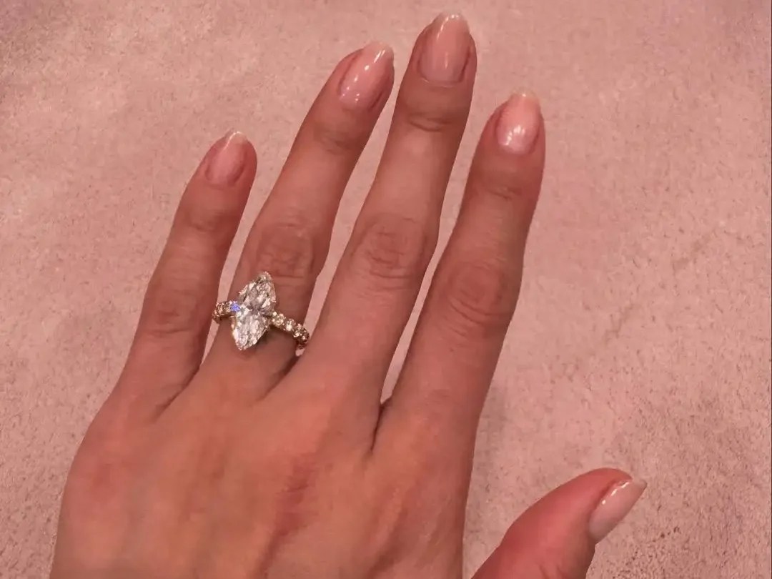 Selena Gomez's hand wearing her engagement ring, with a marquise-cut natural diamond solitaire on a yellow gold eternity band