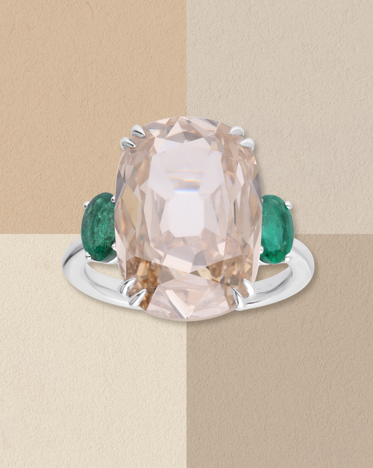 Ring with a large light brown diamond flanked by green gemstones.